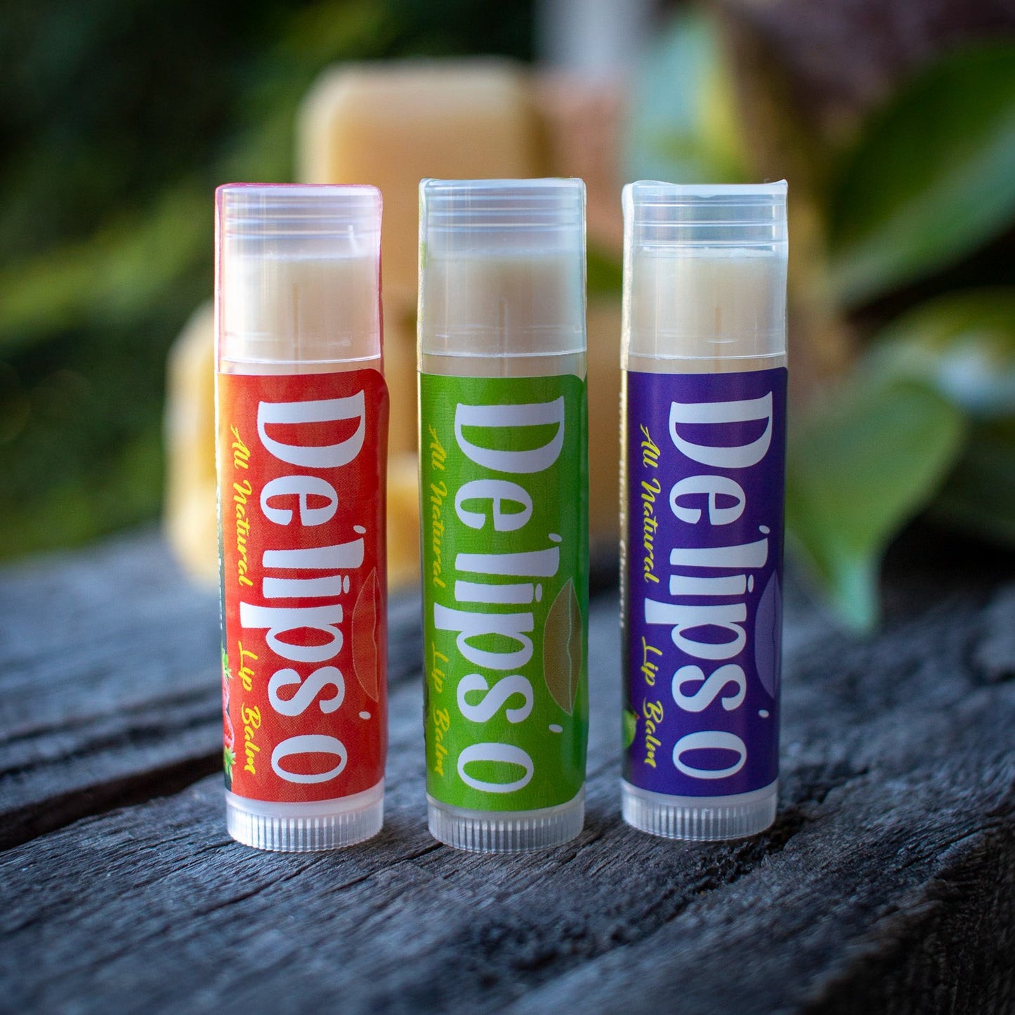 Three lip balm tubes from Delipso on a wooden surface with a blurred natural background
