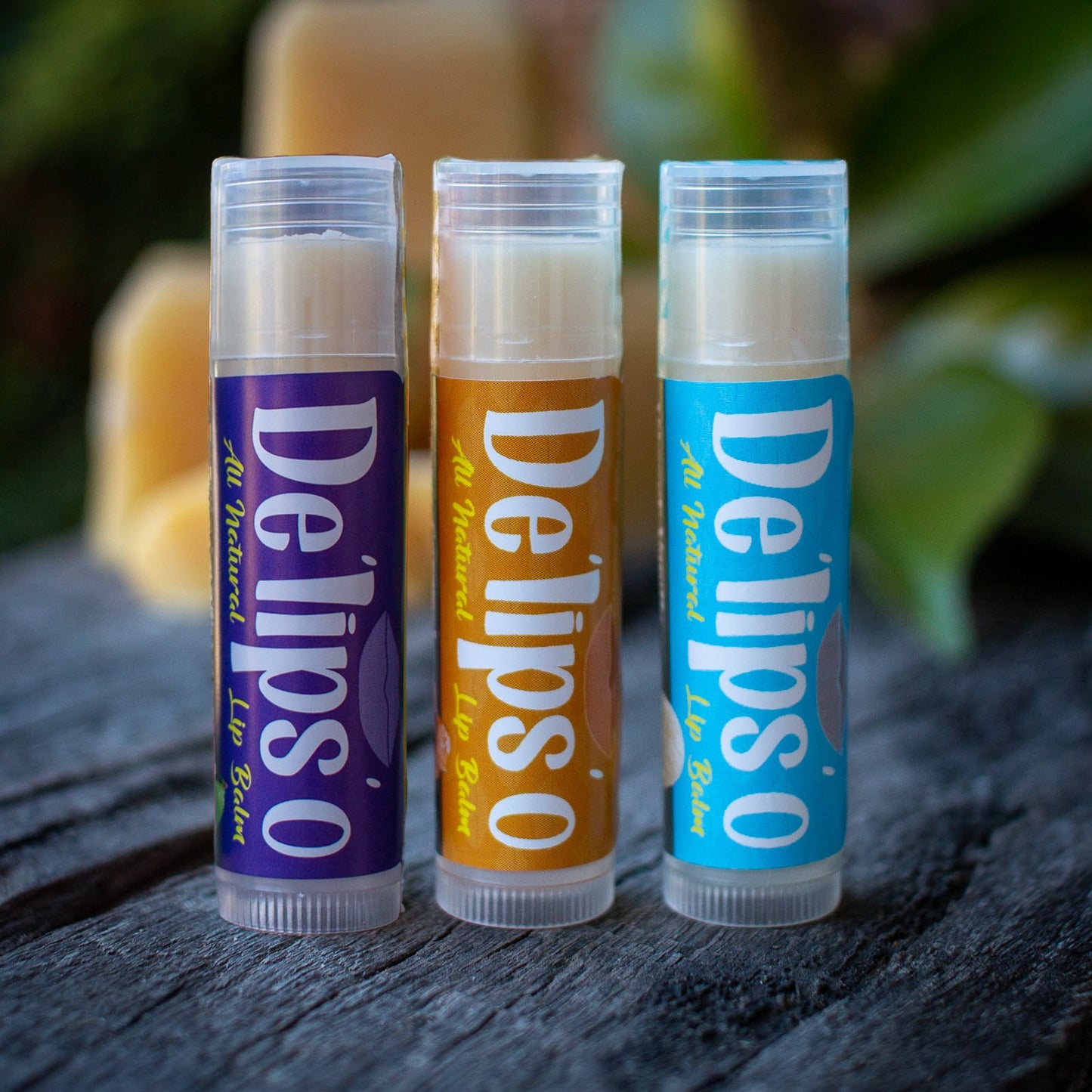 Three Delipso lip balms on a wooden surface with a blurred natural background.