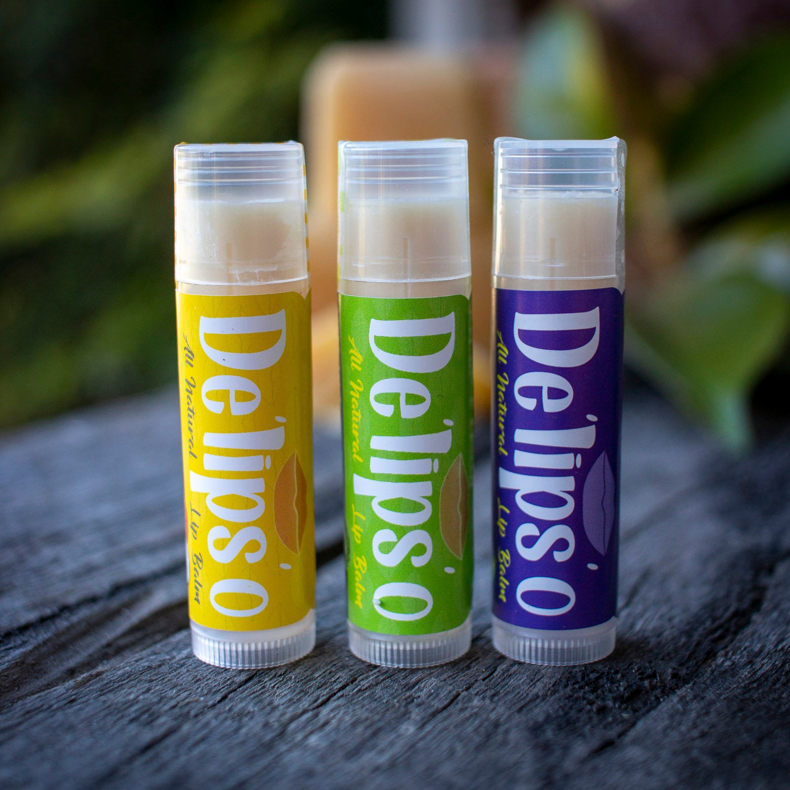 Three lip balms from Delipso on a wooden surface with a blurred natural background
