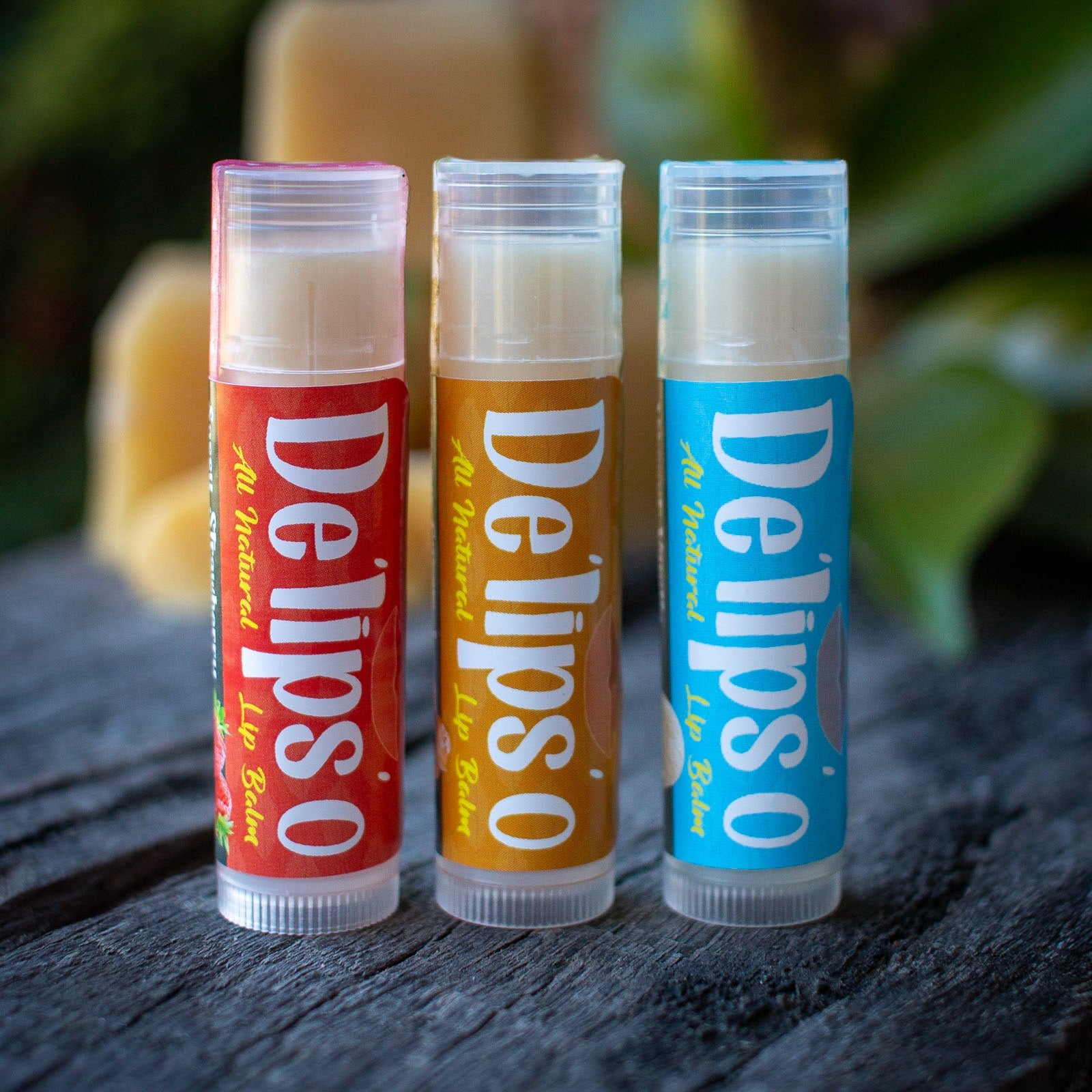 Three lip balm tubes from Delipso on a wooden surface with a blurred natural background.