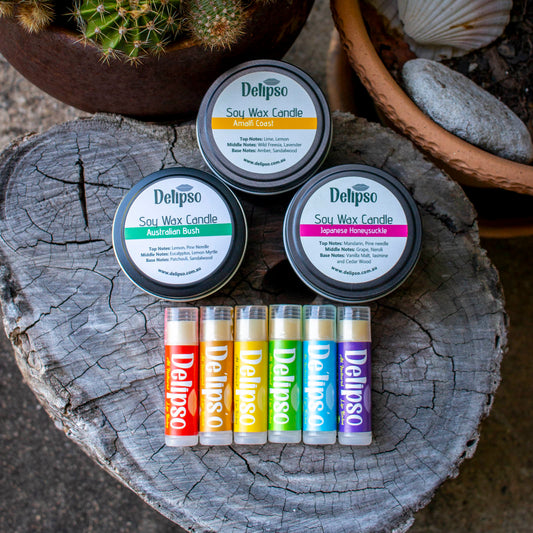 Delipso soy wax candles and lip balms in various scents on a wooden surface with a cactus in the background.