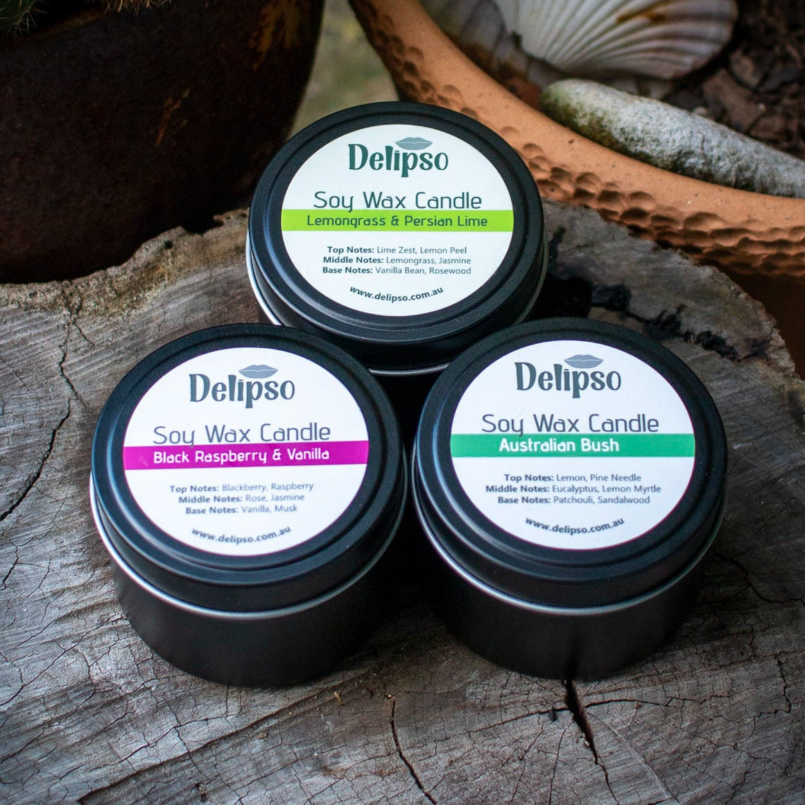 Three Delipso soy wax candles on a wooden surface with plants in the background