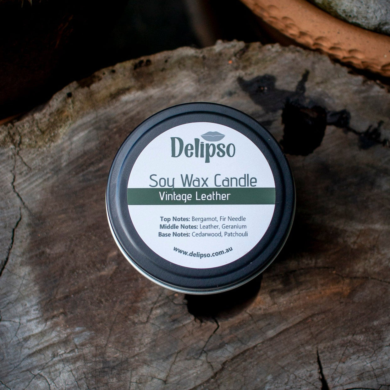 Delipso soy wax candle container on a wooden surface with plants in the background